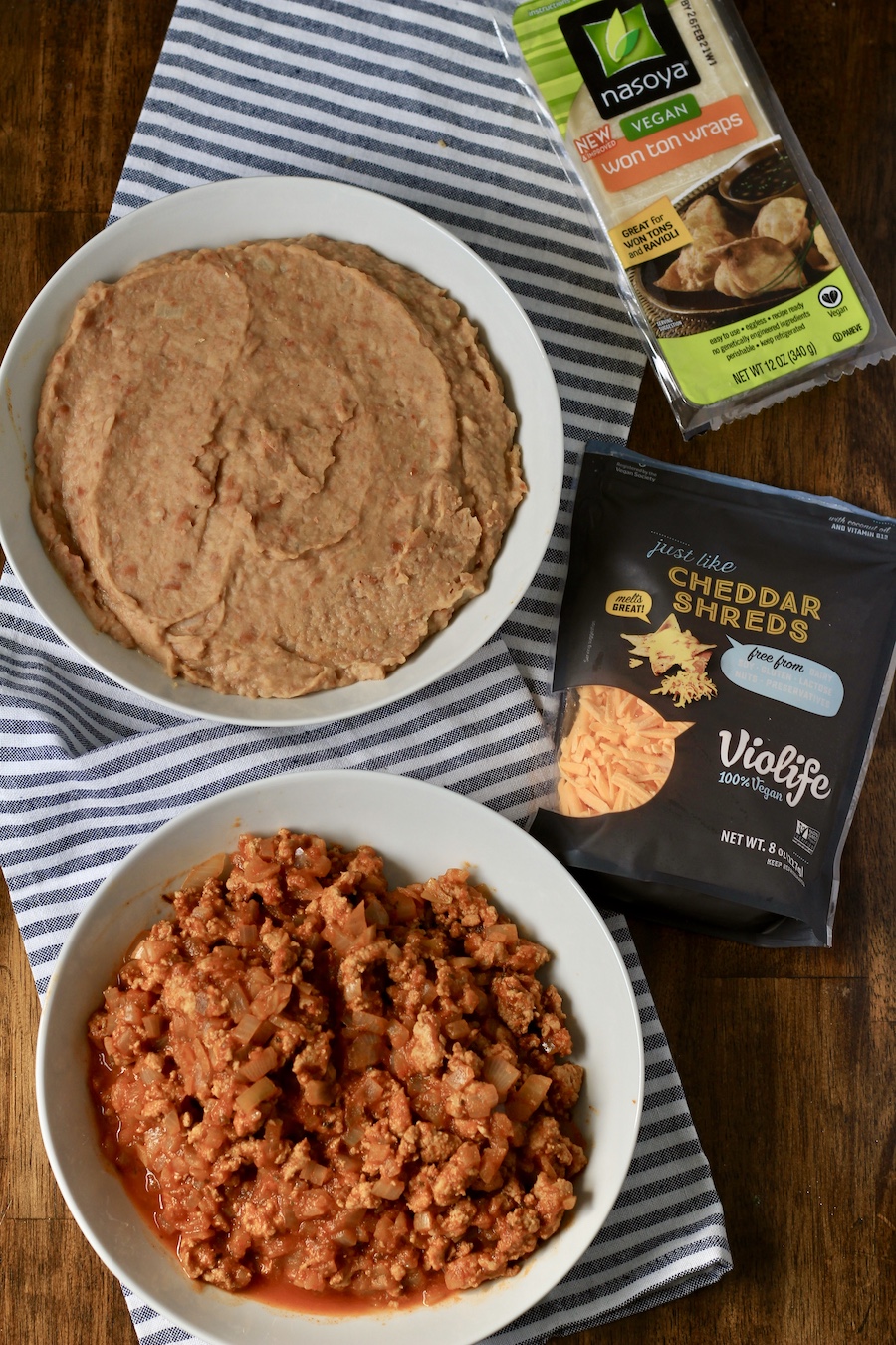 Ingredients for taco cups in bowls on a white and blue dish towel.