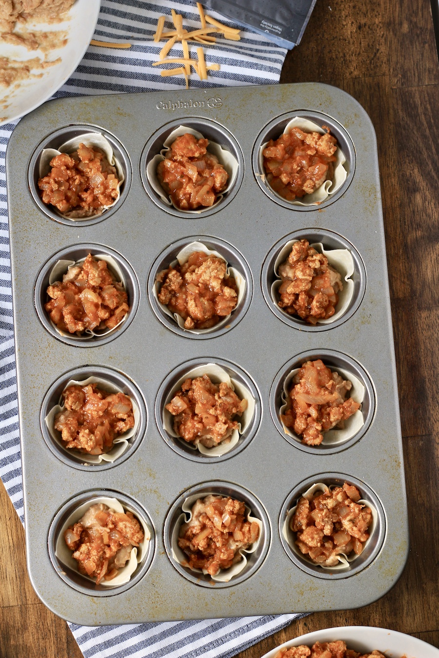 Wonton wrappers topped with beans and taco meat in a muffin time on a wooden counter.