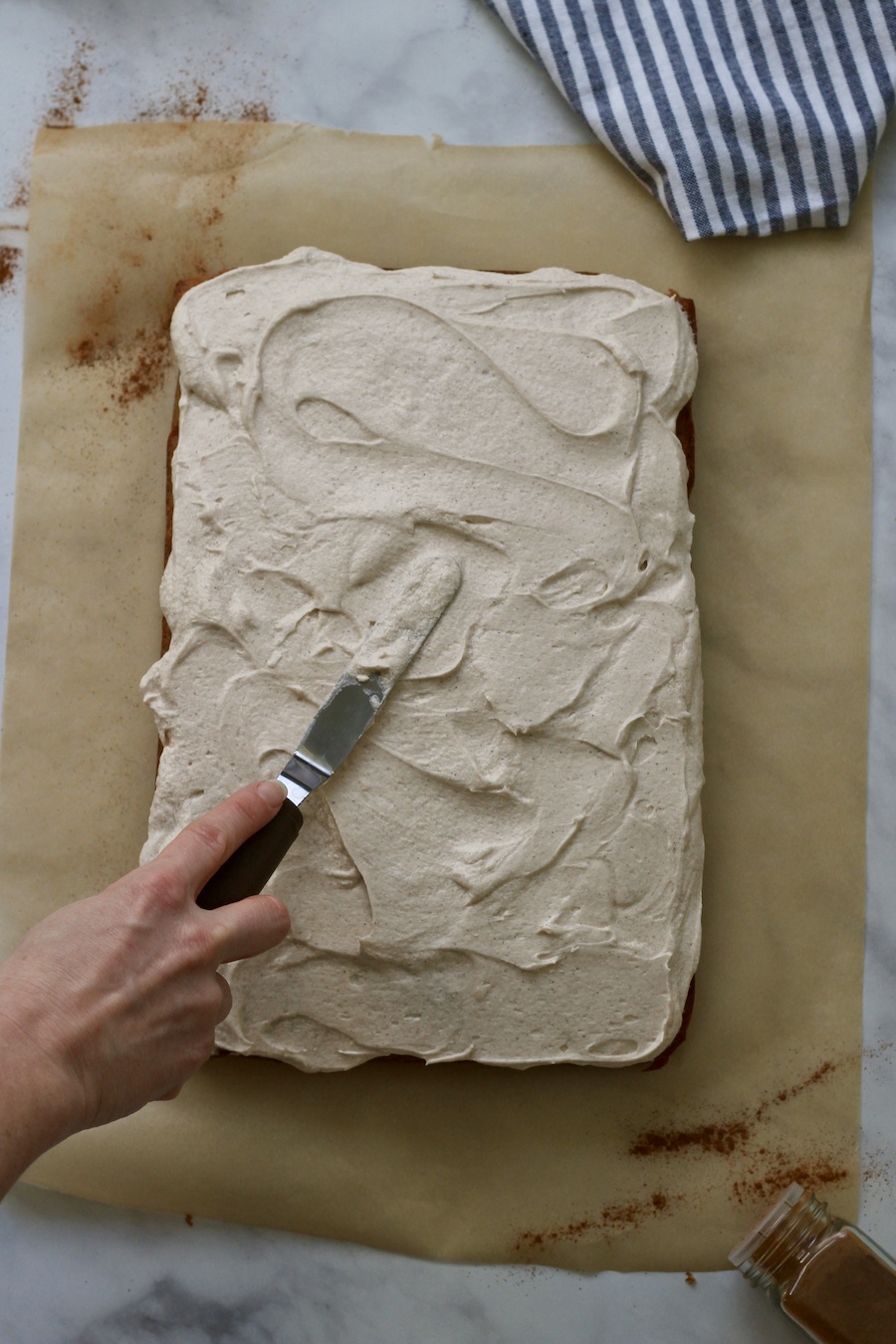 A hand spreading frosting on top of banana slab cake.
