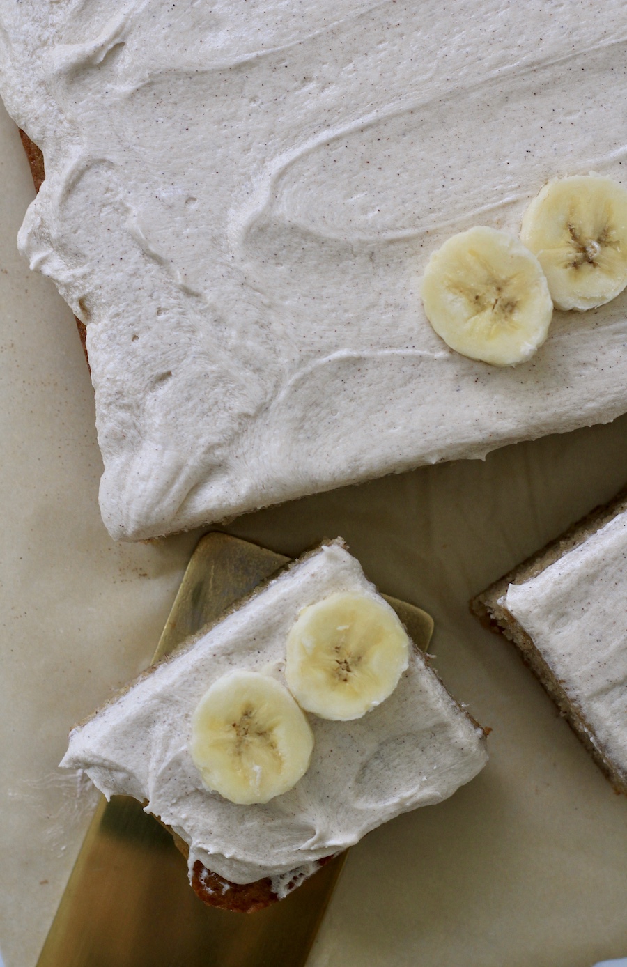 A top down photo of banana slab cake slices on parchment paper with a gold cake server.