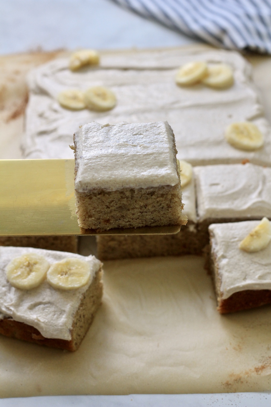 Banana slab cake on a gold cake server with other slices in the back.