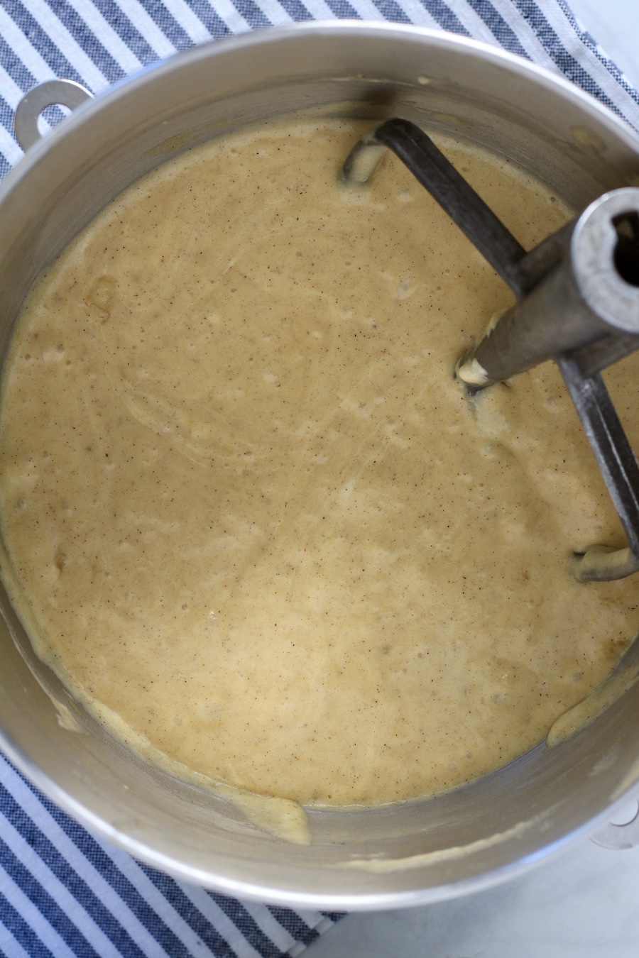 A silver mixing bowl with a paddle with cake batter.