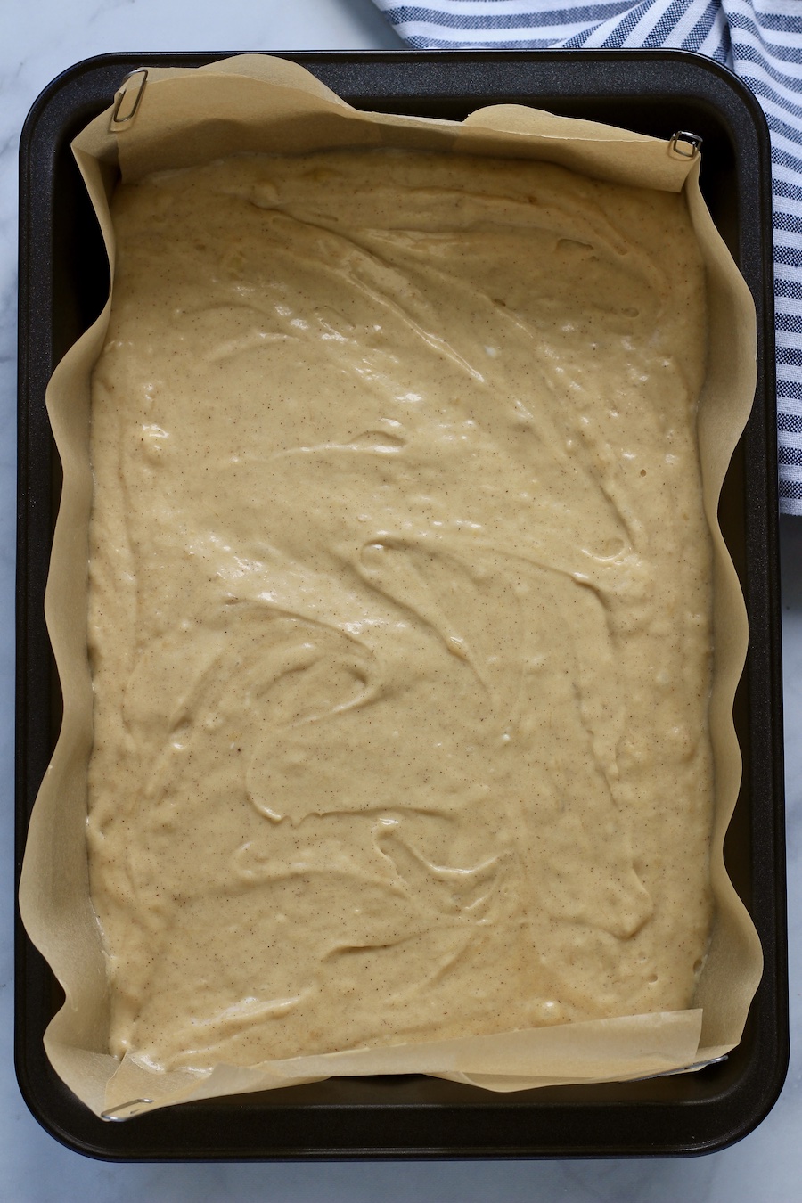 A rimmed cake pan lined with parchment paper filled with cake batter.