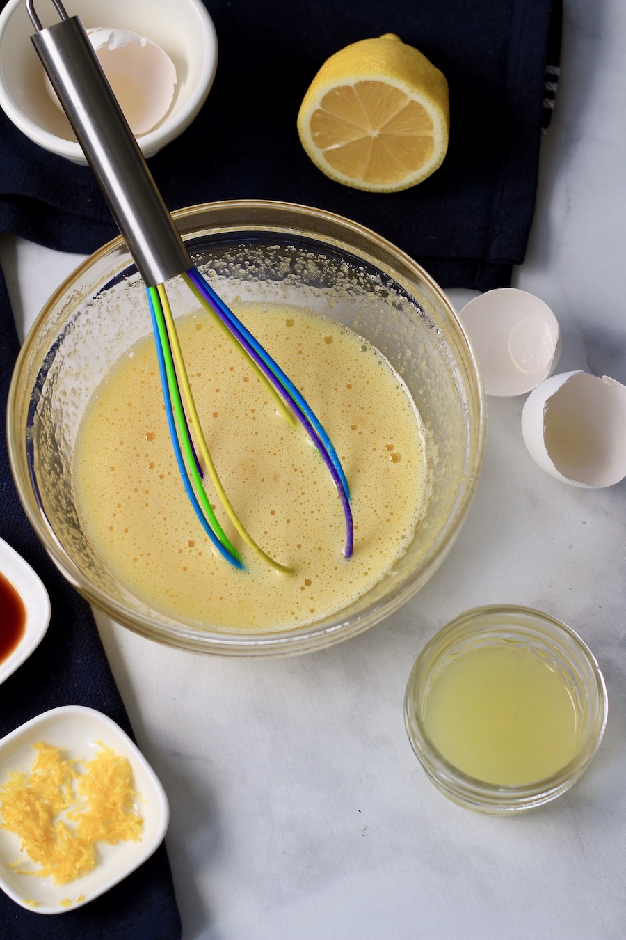 A bowl with a whisk with egg whisked and other ingredients around the bowl.