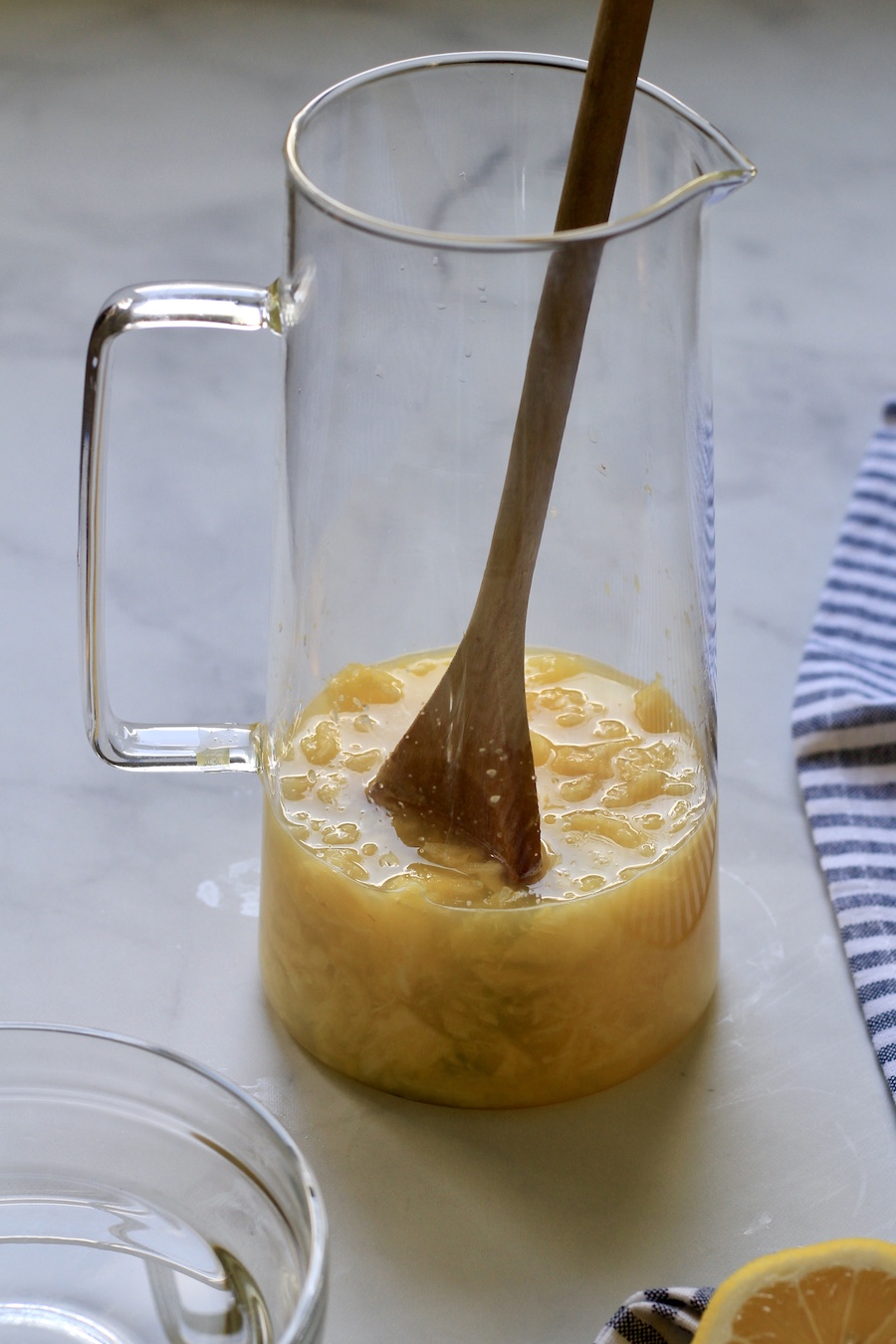 Lemon juice and muddled pineapple mixed together with a wooden spoon in a pitcher.