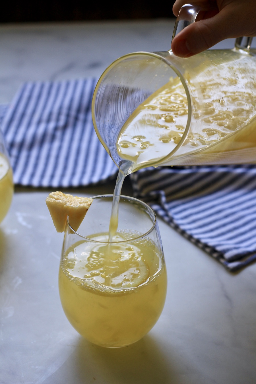 A hand pouring a glass of pineapple lemonade into a glass.