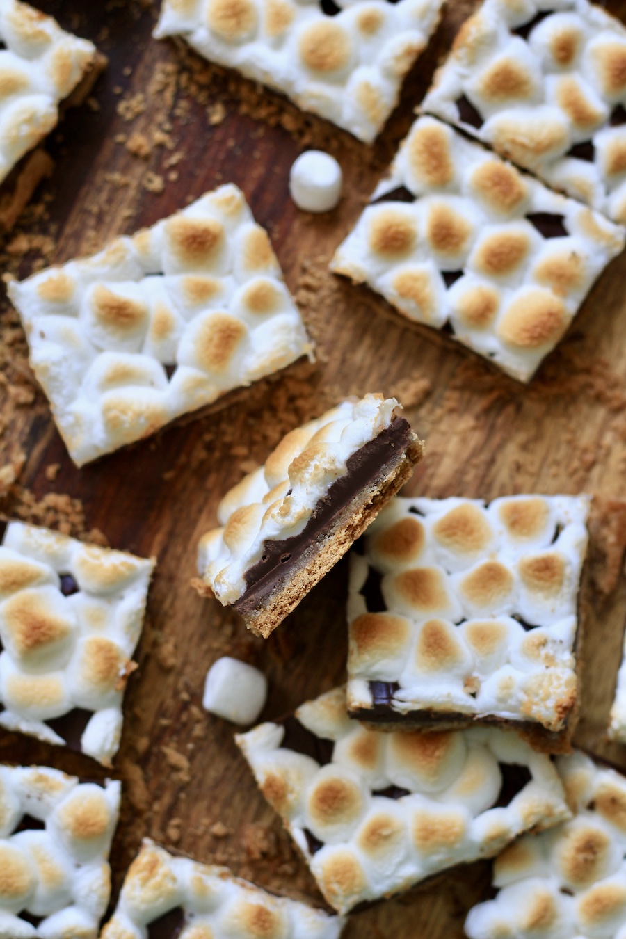 A wooden cutting board with pieces of s'mores toffee and a piece of s'mores toffee on its side.