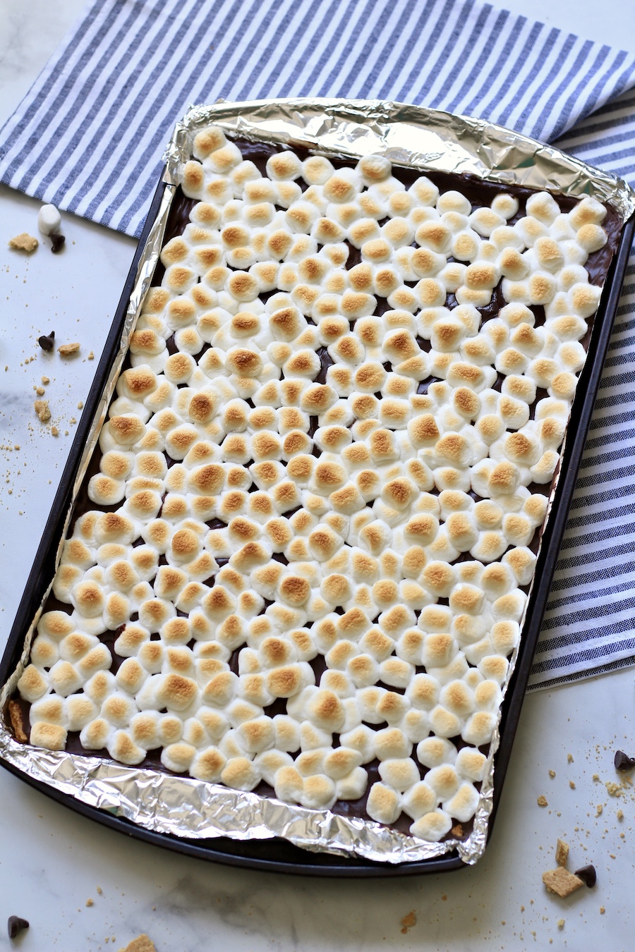 Oven-baked smores toffee lined with foil on a blue and white striped towel.