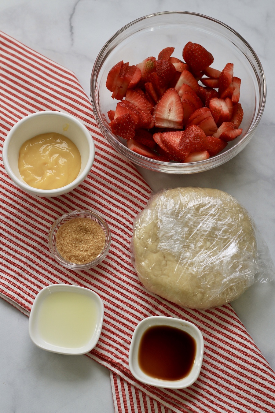 The ingredients for strawberry lemon galette on a counter with a white and red striped towel.
