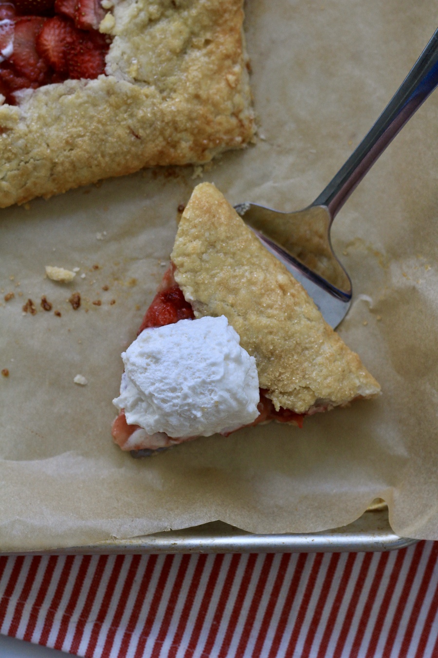 A silver pie server with a slice of strawberry lemon galette with a scoop of whipped topping.