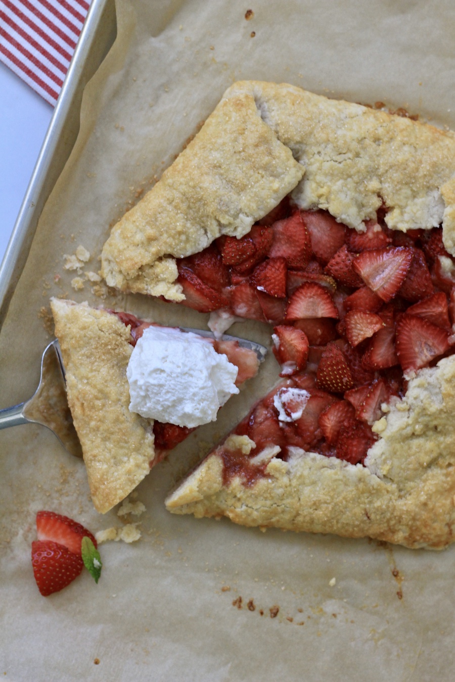 Strawberry lemon galette with a slice cut out in the bottom left topped with a whipped topping on a parchment paper lined baking sheet.