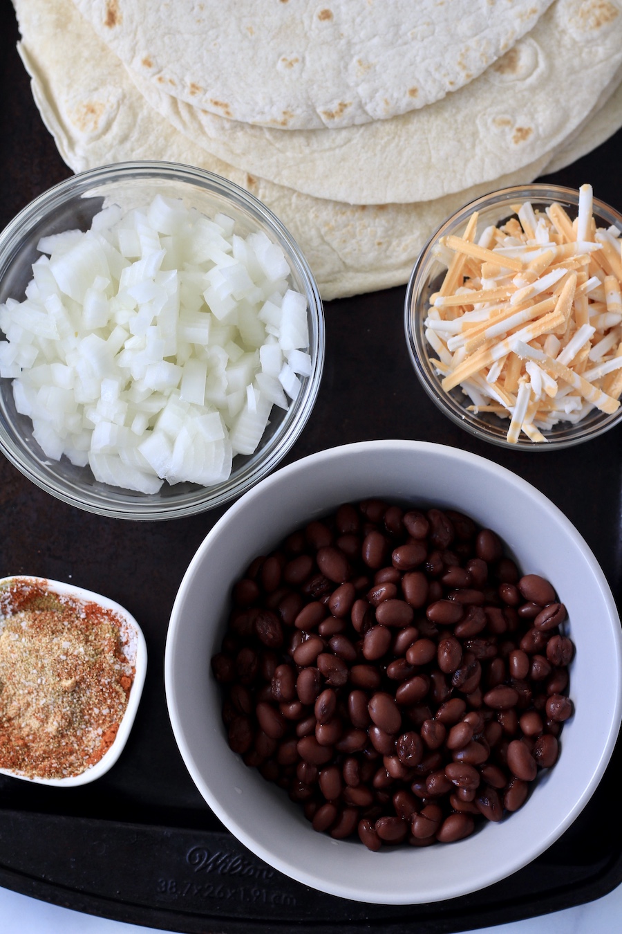 A rimmed baking sheet with the ingredients for vegan black bean and cheese quesadillas.