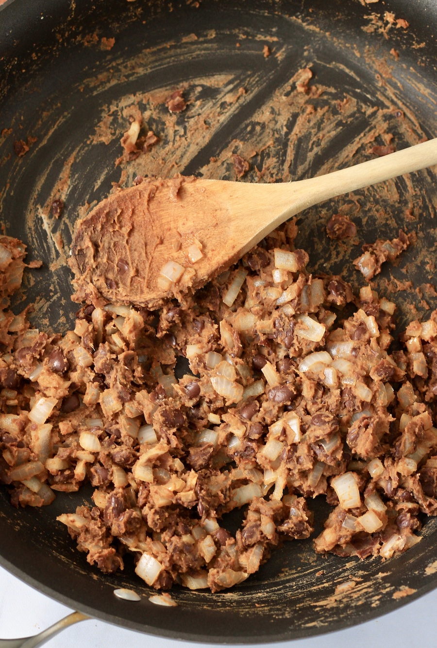 A skillet with a wooden spoon and smashed vegan black bean filling.