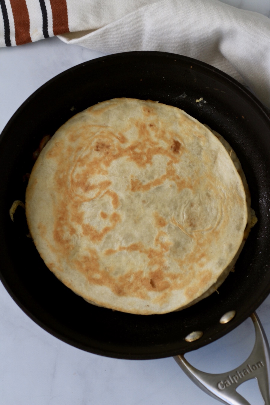 A skillet with a fully cooked vegan black bean and cheese quesadilla.