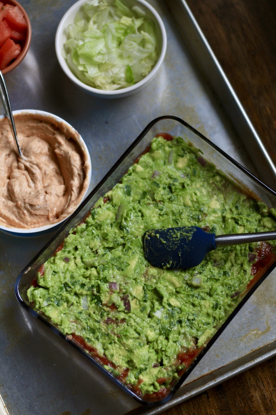 A layer with the guacamole in the glass dish with a spatula.