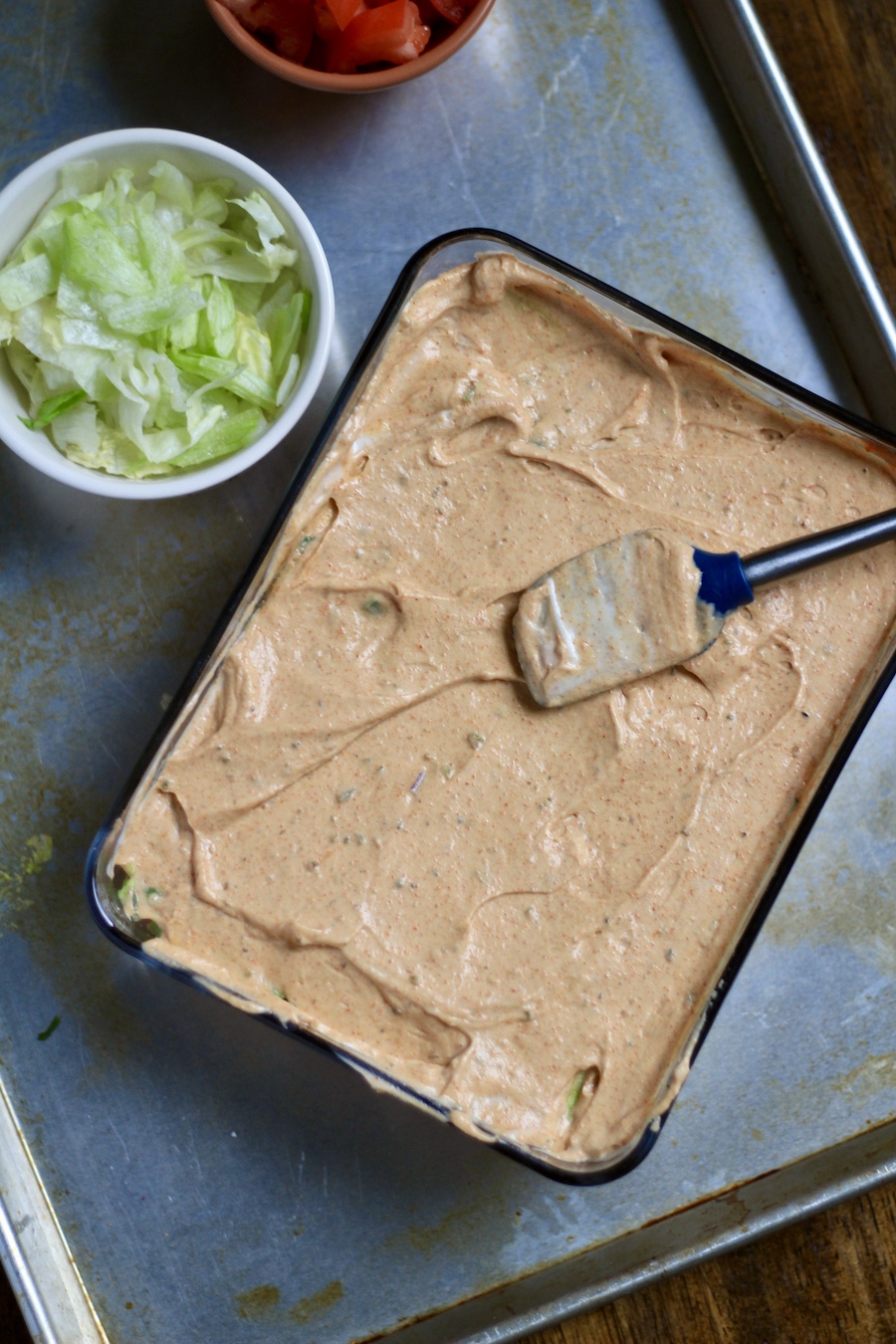 The sour cream layer spread in the glass dish topped with a spatula.