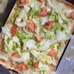 A top down photo of vegan 7 layer dip with shredded lettuce and diced tomato.