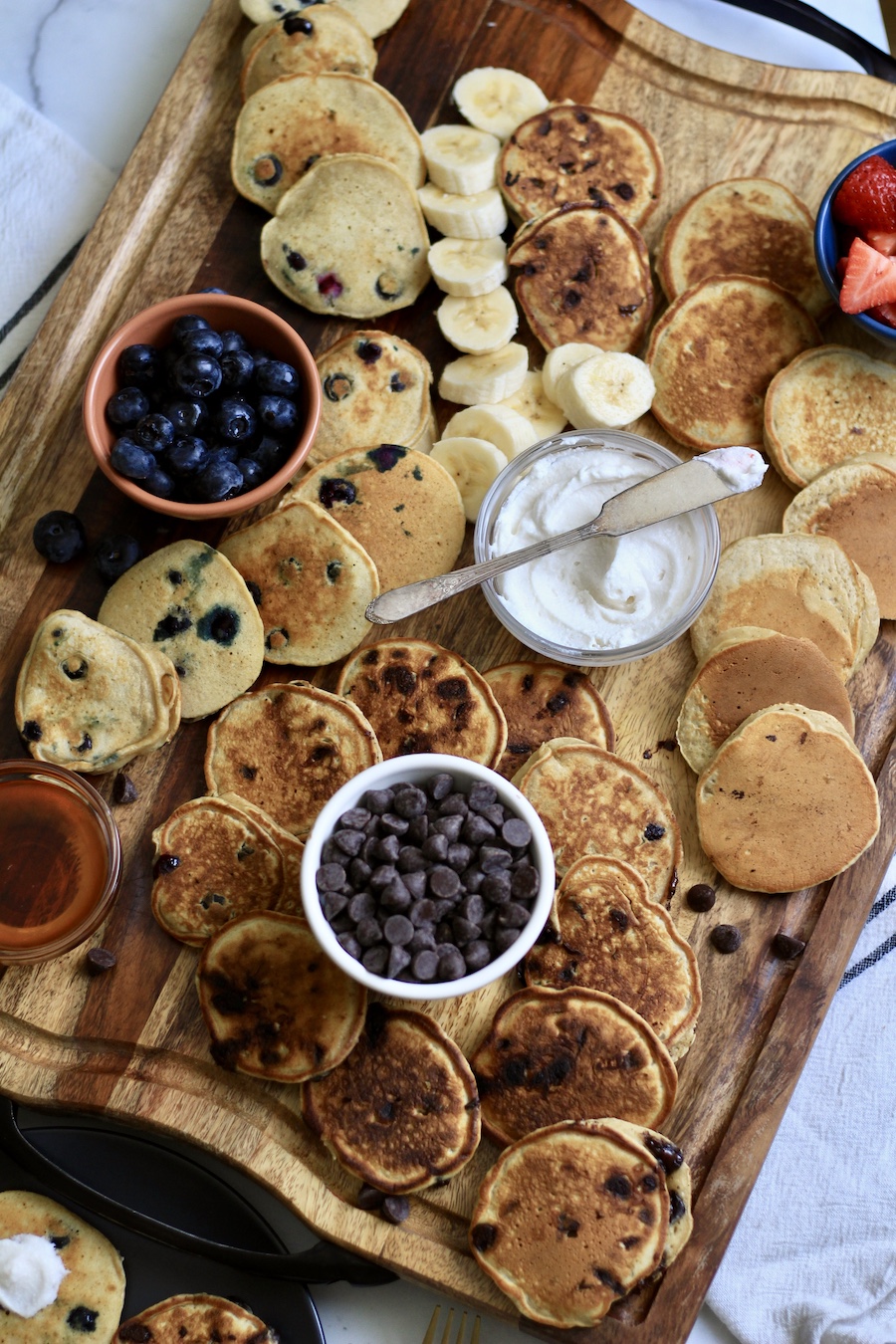 A dairy-free pancake board with mini buttermilk pancakes and a little knife on top of a bowl of dairy-free whipped topping.