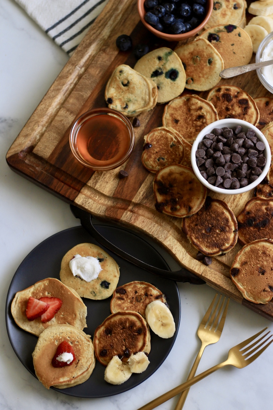 A small blue plate with mini buttermilk pancakes and two gold forks to the left with a pancake board above.
