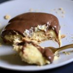 A blue plate with a white plate on top with a slice of chocolate eclair dessert and a fork with a bite on it in front.