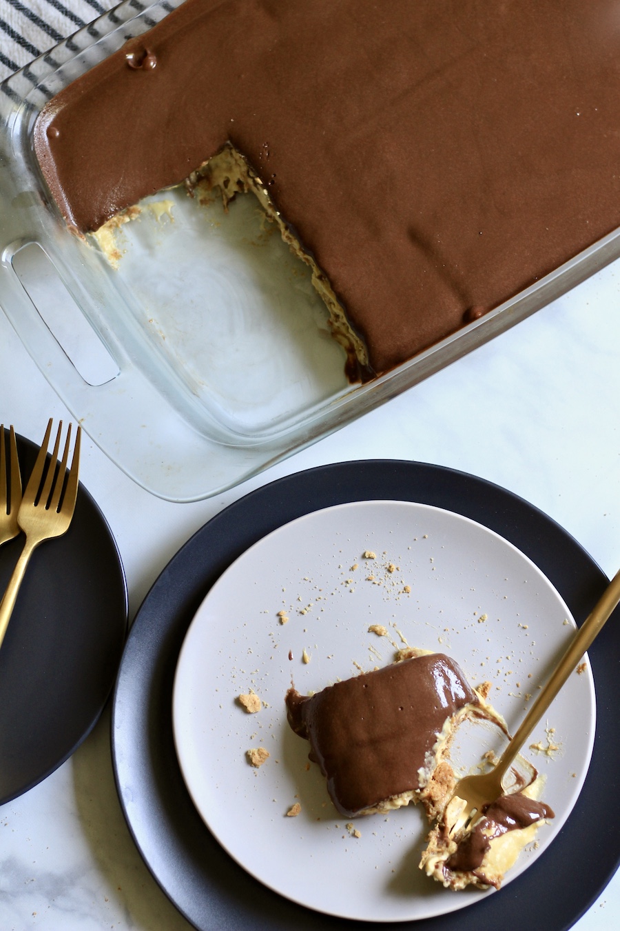 Top down photo of chocolate eclair dessert with a slice on a plate and the pan of dessert in the back.