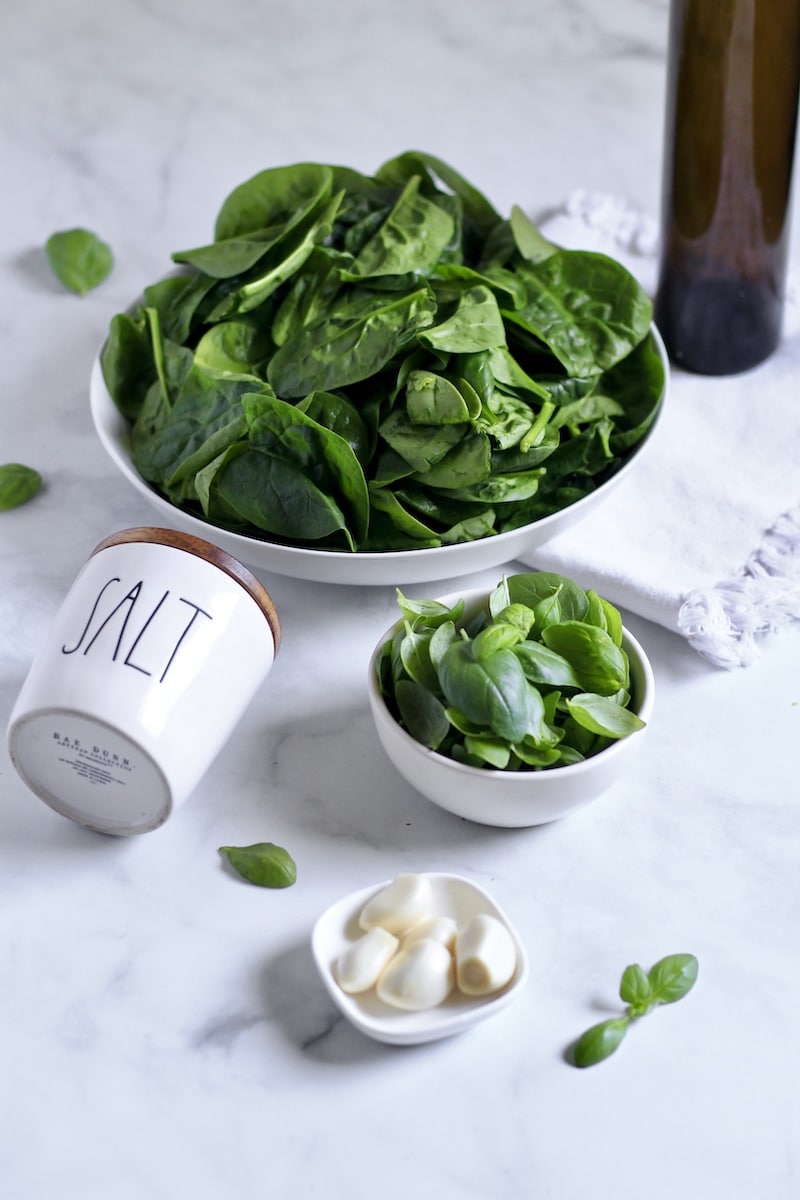 A white counter with the ingredients for spinach pesto in bowls.