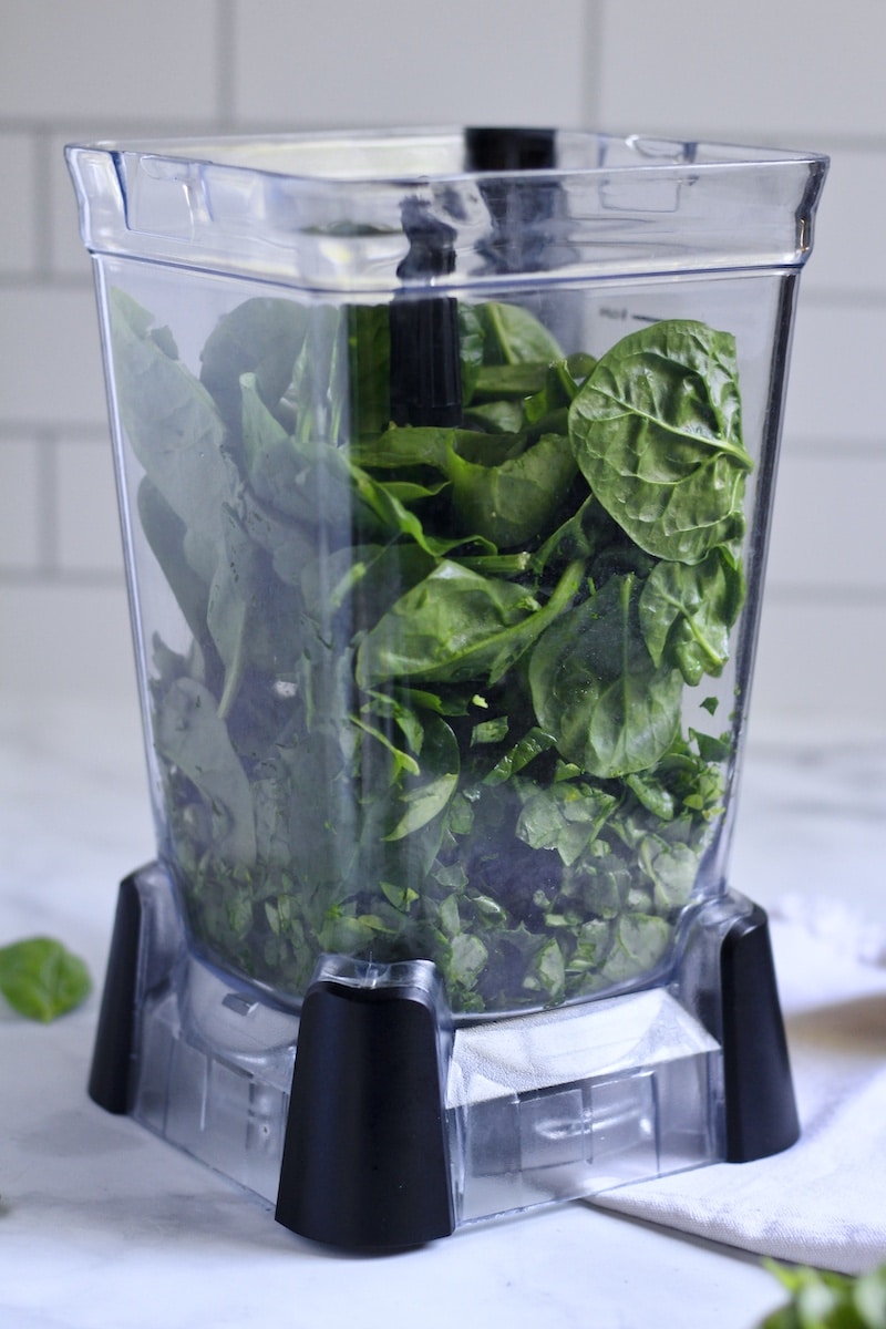 A clear blender with the spinach inside the blender.
