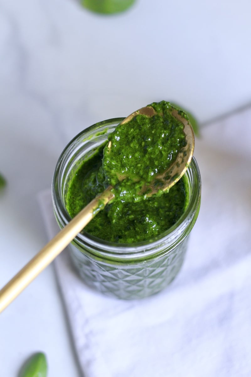 A golden spoon coated in spinach pesto on a white towel.
