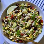 A white bowl of texas caviar pasta salad with wedges of lime and a gold fork.