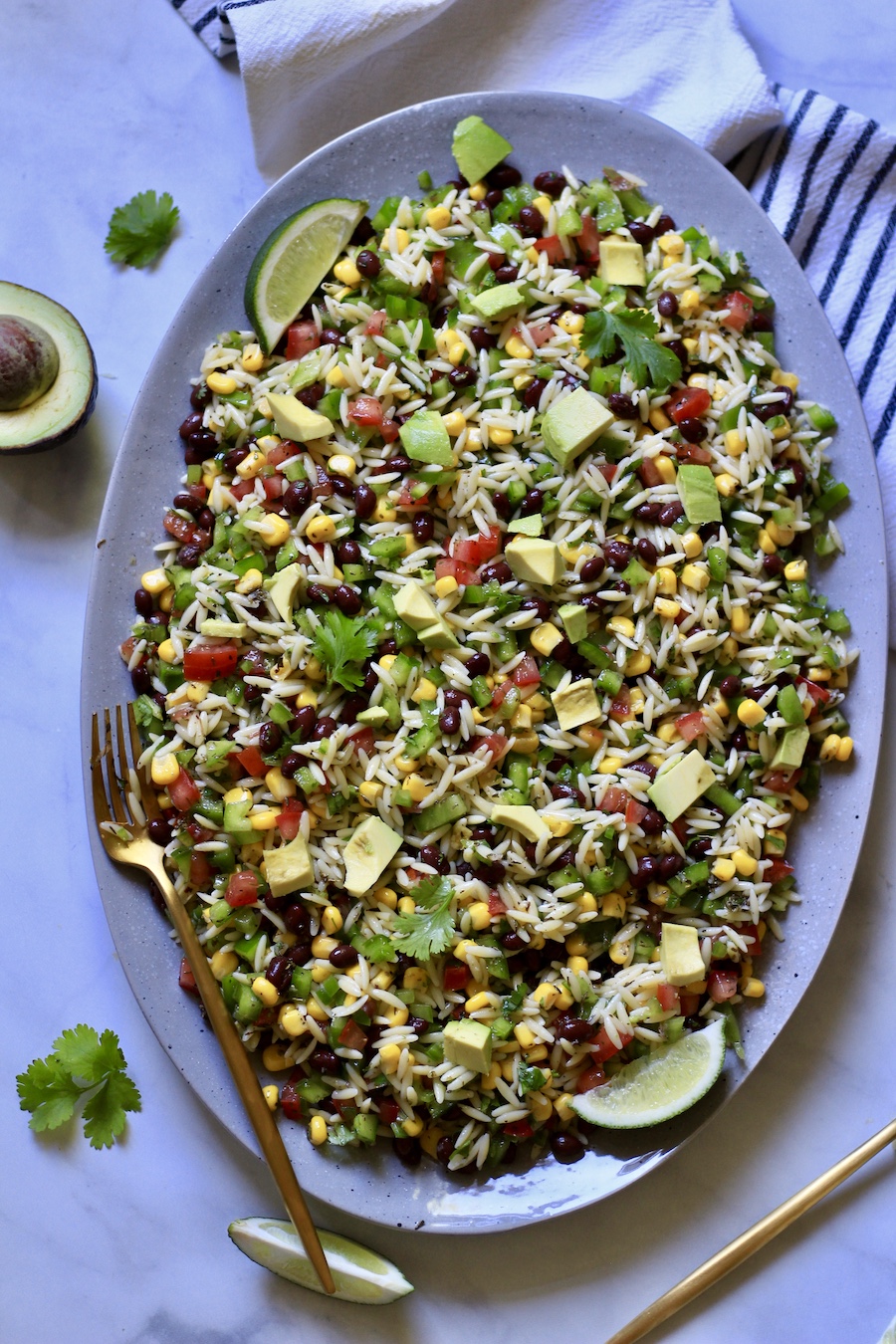 A full blue platter with texas caviar pasta salad with an avocado in the top left and a gold fork on the platter in the bottom right.