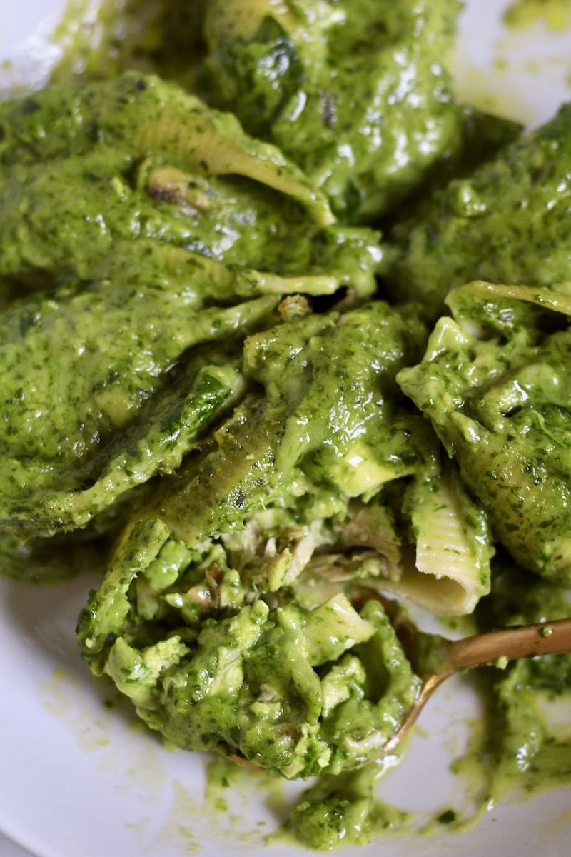 A close up of a chicken pesto stuffed shell with a spoon scooping a bite out.
