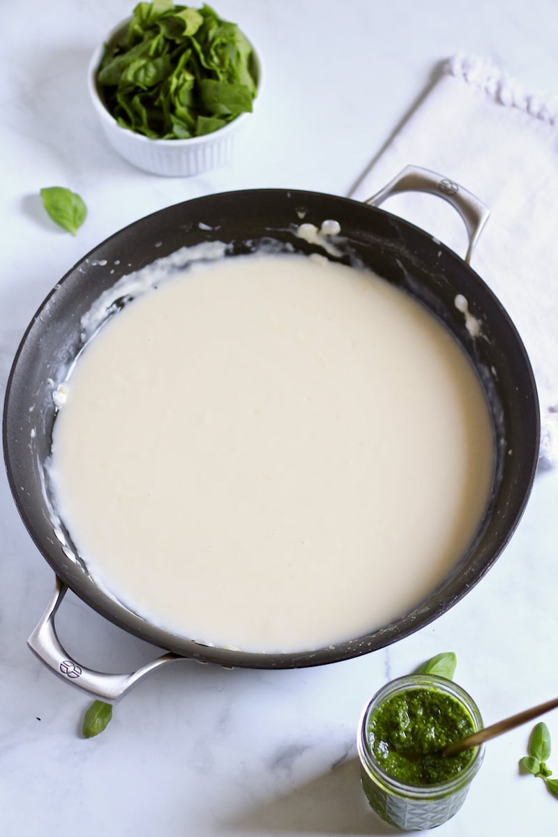 A non-stick skillet with the base of the pesto cream sauce on a white counter.