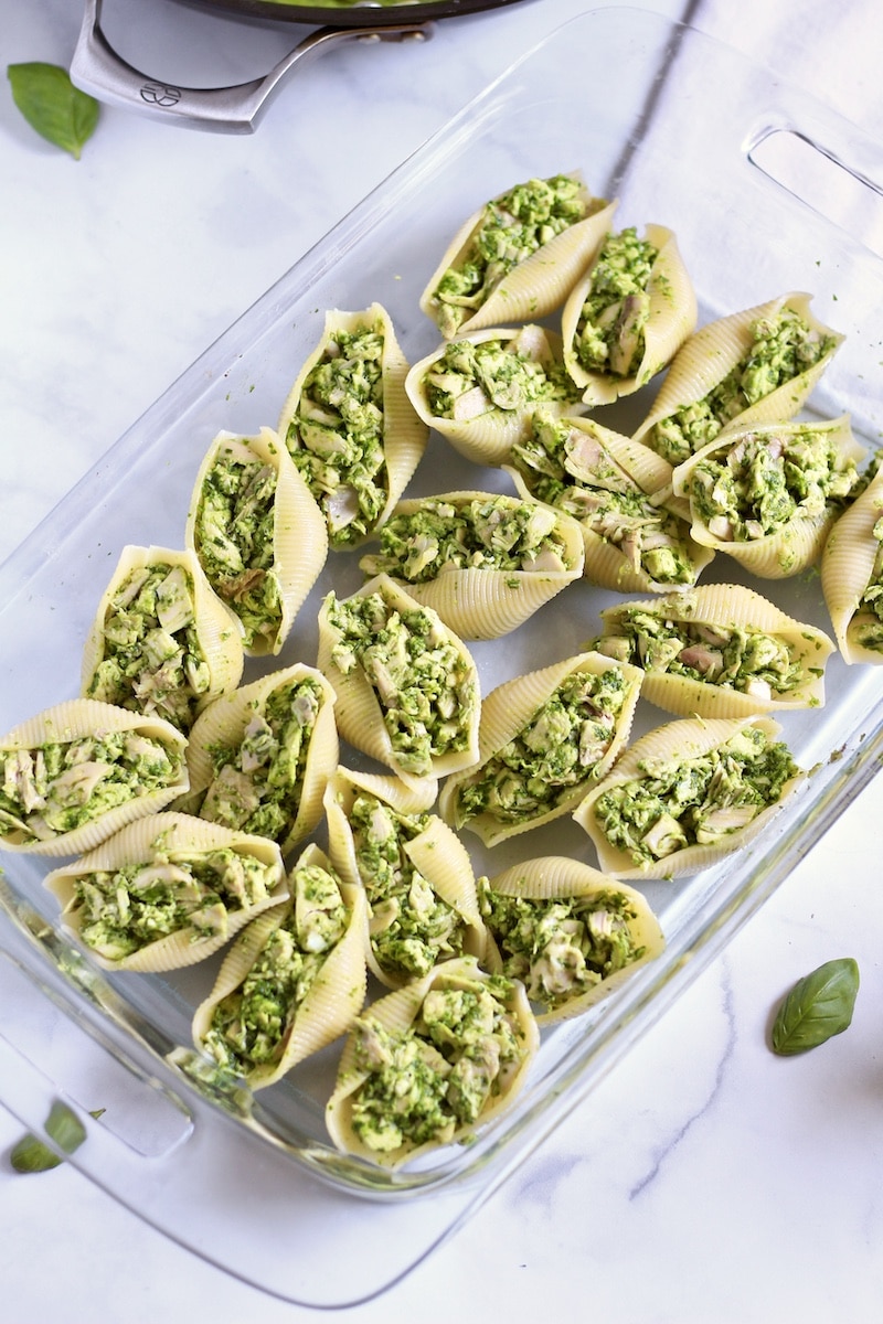 A glass baking dish with large pasta shells stuffed with pesto shredded chicken.