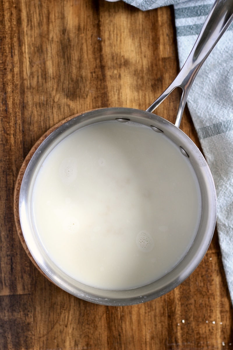 A top down photo of the milk and water boiling in a saucepan on a wooden counter.