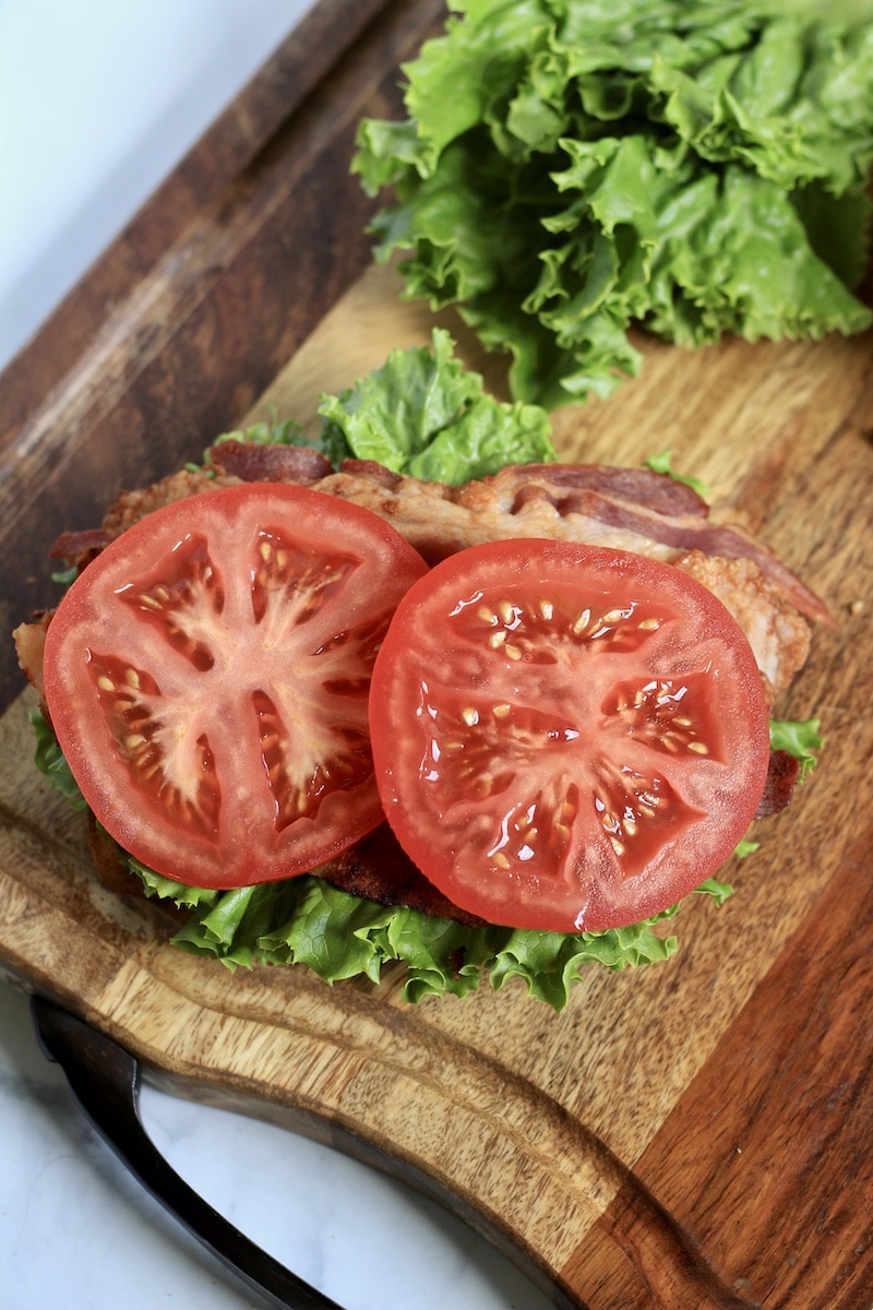 A top down photo of the tomatoes on top of the bacon on a wooden cutting board.