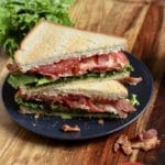 Two triangle cut pesto blt sandwiches on a blue plate on a wooden cutting board.