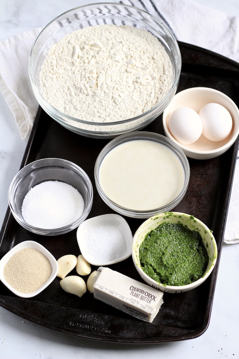 Ingredients for pesto rolls on a dark baking sheet with a whtie and blue dish towel in the back.