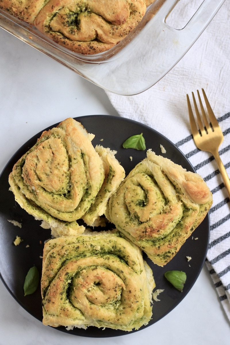 A blue plate with three pesto rolls a fork to the right and a glass baking dish of pesto rolls in the back.