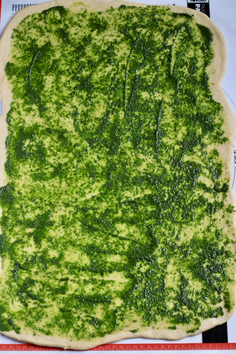 Rolled out bread dough topped with pesto.