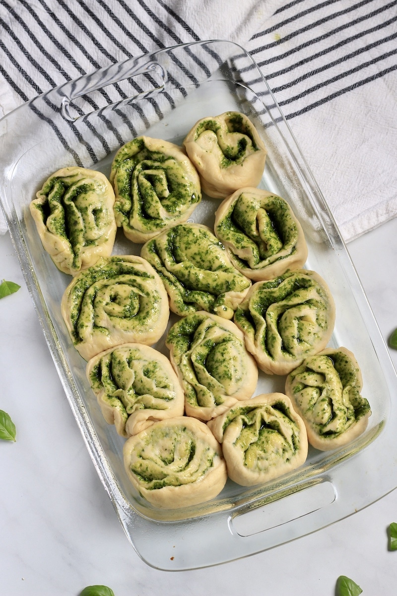 A glass baking dish with 12 pesto rolls before rising.