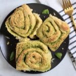 A square photo with a blue plate with three pesto rolls and a gold fork to the right.