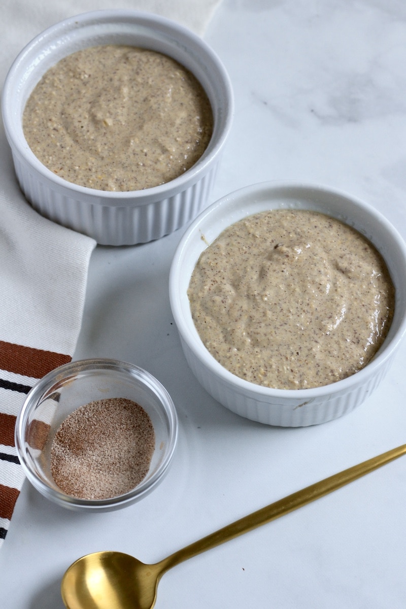 Top down photo of two ramekins with snickerdoodle baked oats and cinnamon sugar in a small bowl in the front.
