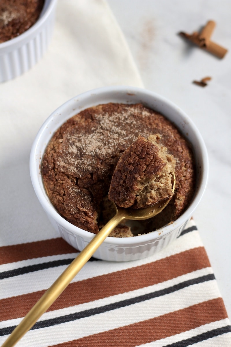 Top down photo of a gold spoon scooping out a bite of snickerdoodle baked oats in a white ramekin on a white and orange striped towel.