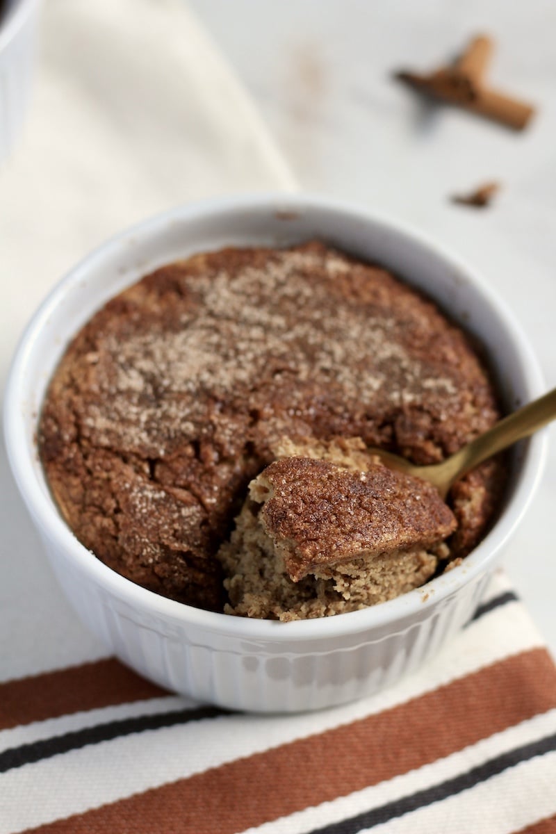 A from the side photo of snickerdoodle baked oats in a white ramekin with a gold spoons and a bite on the spoon.