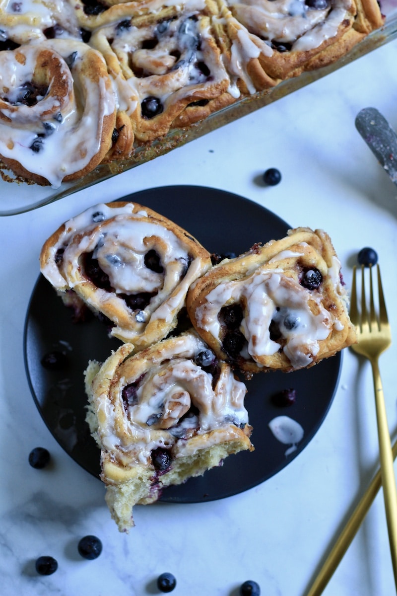 A blue plate with three lemon blueberry sweet rolls on tops and a gold fork to the right.
