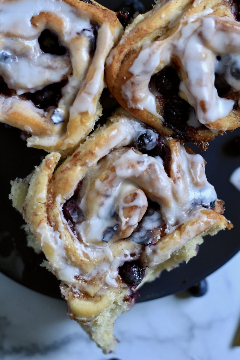 A close up of a lemon blueberry sweet roll on a blue plate.