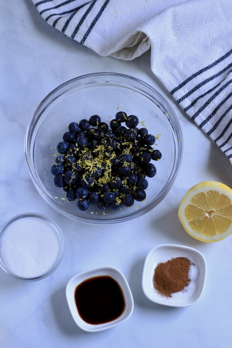 Ingredients for the lemon blueberry filling on a white counter with a blue and white striped towel in the back.