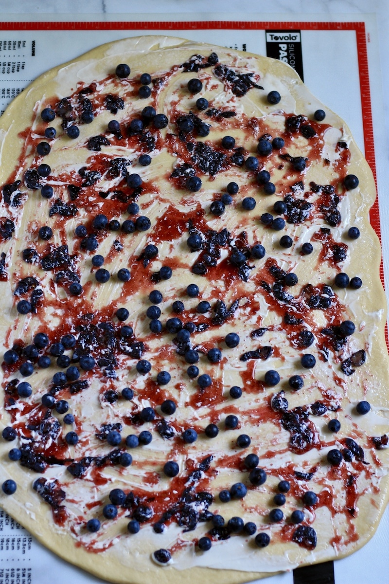 Rolled out sweet roll dough spread with plant-based butter and the blueberry filling.