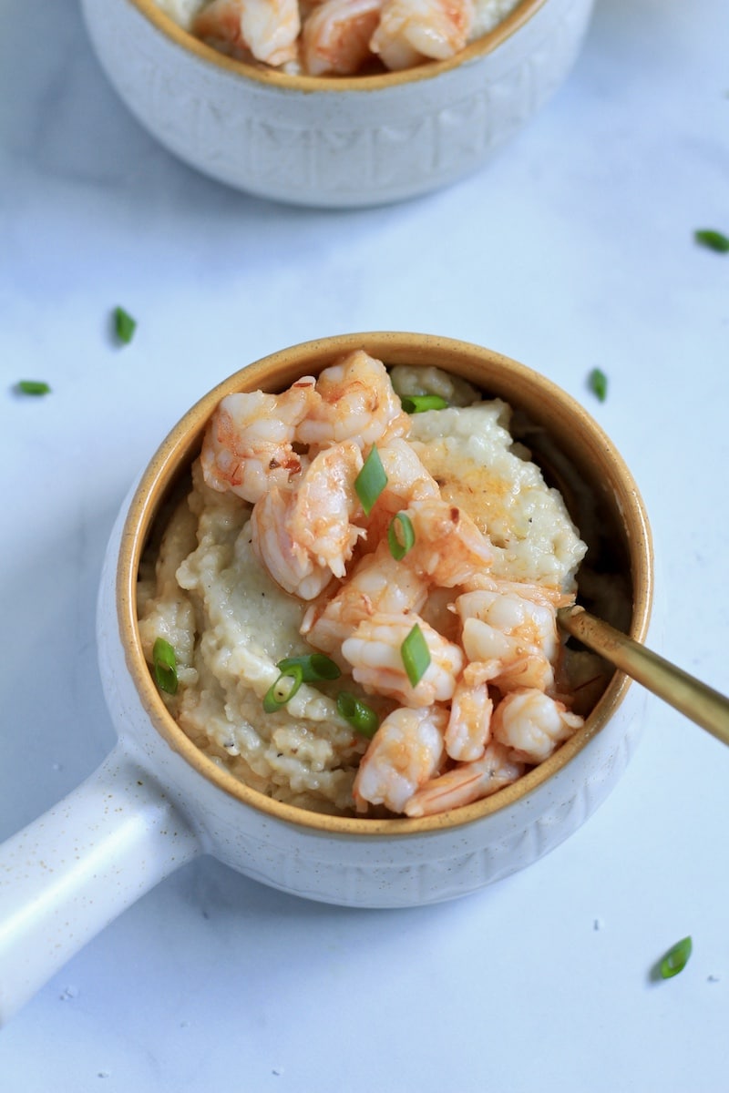 One small orange rimmed bowl with chili garlic shrimp and grits with a gold spoon in the top.