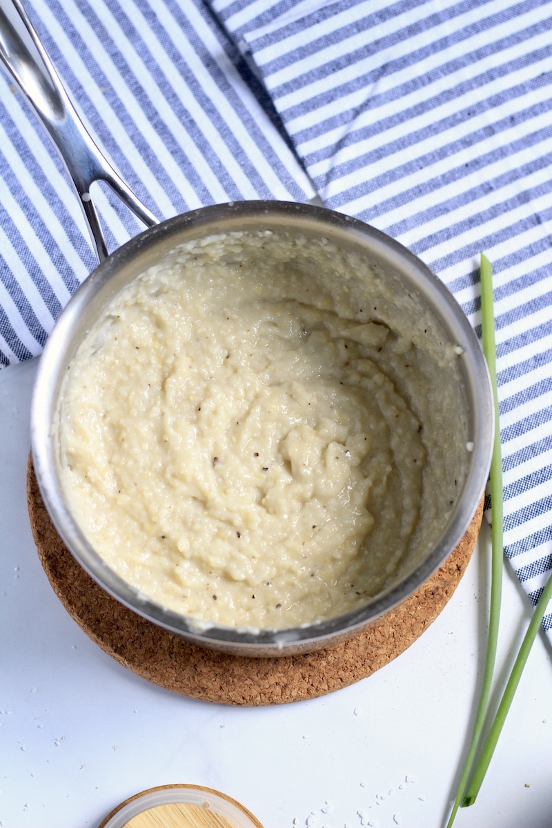 Garlic butter grits mixed in a saucepan with a blue and white striped dish towel in the back.